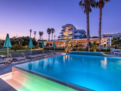 Wieczorny widok na oświetlony basen hotelowy z palmami i leżakami.