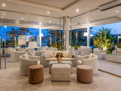 Nowoczesny, jasny kącik wypoczynkowy w hotelu z sofami, stołkami i dużymi oknami z widokiem na palmy.