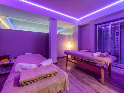 Relaxační wellness místnost se dvěma masážními lehátky, fialovou atmosférou a jemným osvětlením.