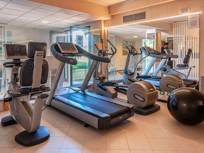 Jasna siłownia z różnym sprzętem treningowym i dużymi lustrami na ścianie.