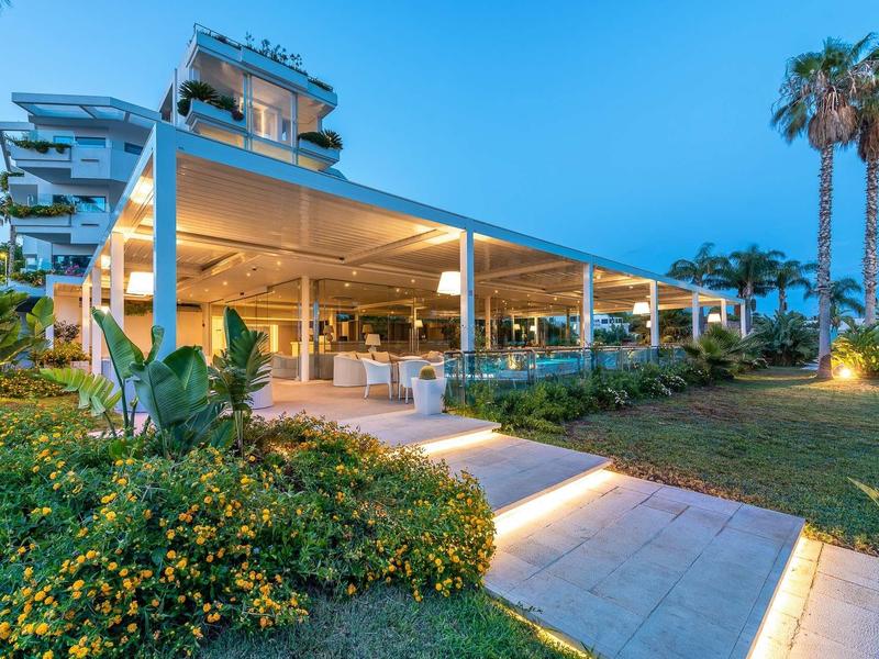 Moderní hotelová restaurace s osvětlenými cestičkami a upravenými zahradami za soumraku.