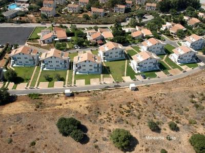 Fila di sei case bianche con giardini lungo una strada, circondate da terreno secco.