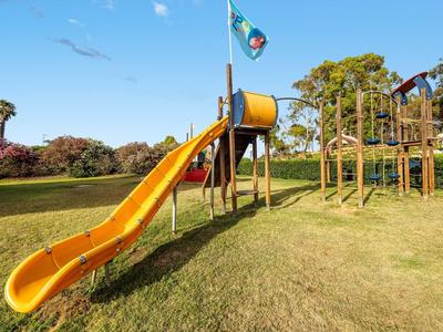Duża żółta zjeżdżalnia na słonecznym placu zabaw z drabinką do wspinaczki i flagą.