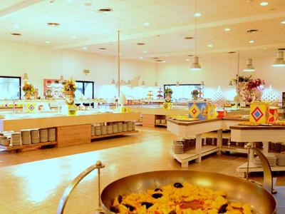 Jasna, nowoczesna restauracja bufetowa z okrągłymi wyspami kuchennymi i różnorodnymi potrawami.