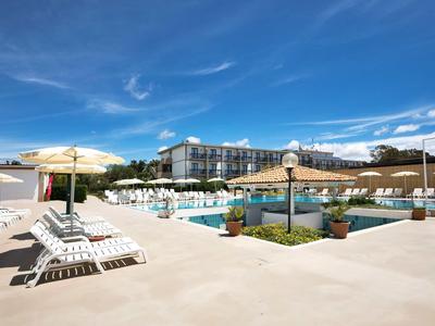 Area piscina dell'hotel con lettini, ombrelloni e edificio moderno sotto un cielo azzurro