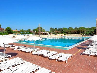 Duży basen hotelowy z białymi leżakami i parasolami pod bezchmurnym niebem.