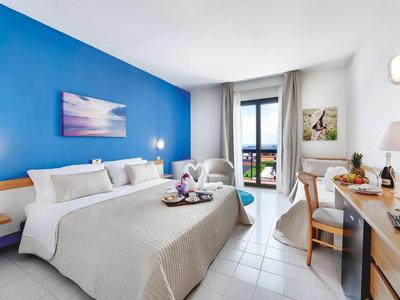 Jasny pokój hotelowy z dużym łóżkiem, biurkiem i balkonem z widokiem.