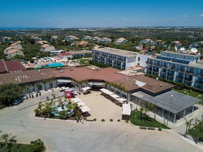 Widok z lotu ptaka na ośrodek z basenem, terenami zewnętrznymi i okolicznym pejzażem miejskim.