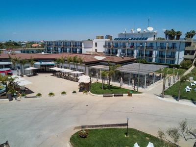 Moderner Hotelkomplex mit weißem Gebäude, Sonnenschirmen, Poolbereich und klar blauem Himmel.