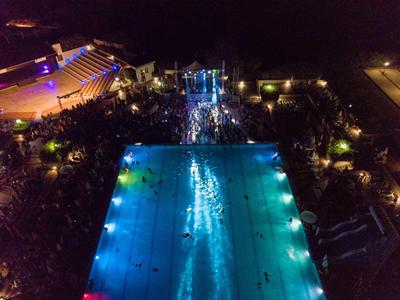Piscina illuminata di notte con ospiti e area eventi