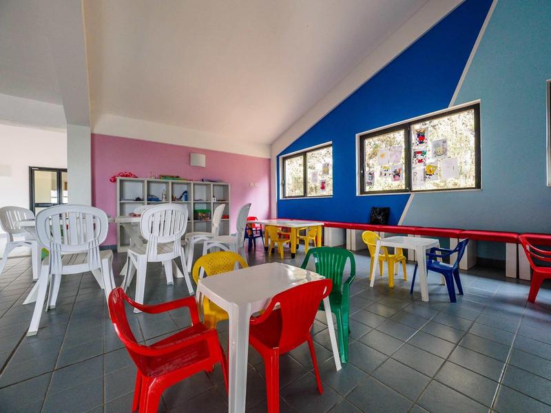 Kolorowe wnętrze z plastikowymi krzesłami i stołami, niebieskie i różowe ściany oraz podłoga z kafli.