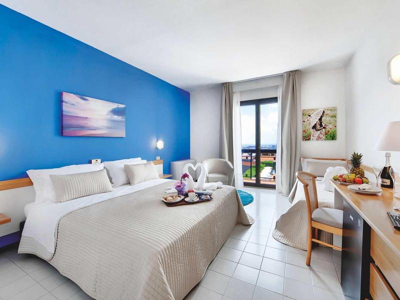 Jasny pokój hotelowy z dużym łóżkiem, biurkiem i balkonem z widokiem.