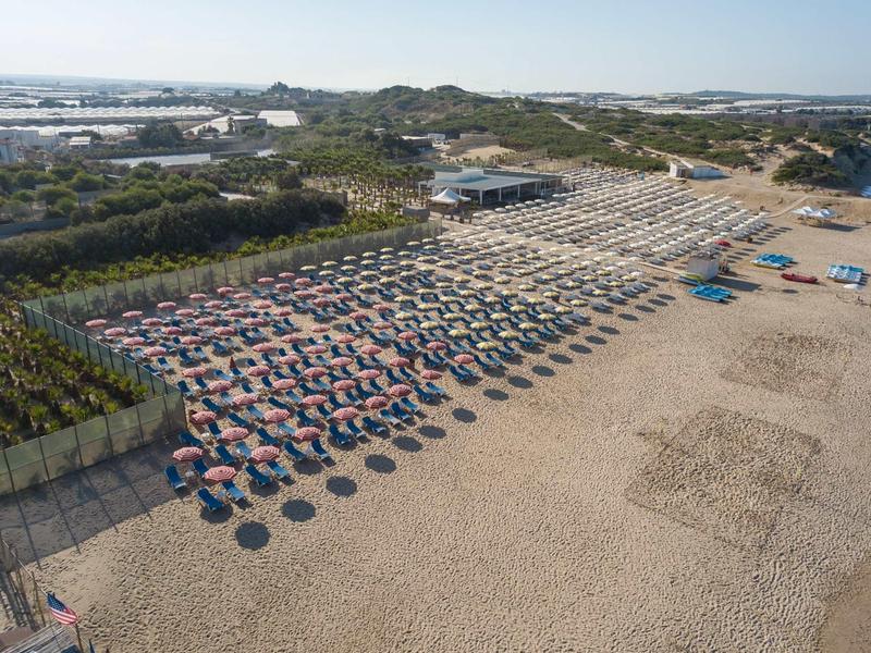 Kilometrowa piaszczysta plaża z uporządkowanymi rzędami parasoli i leżaków.