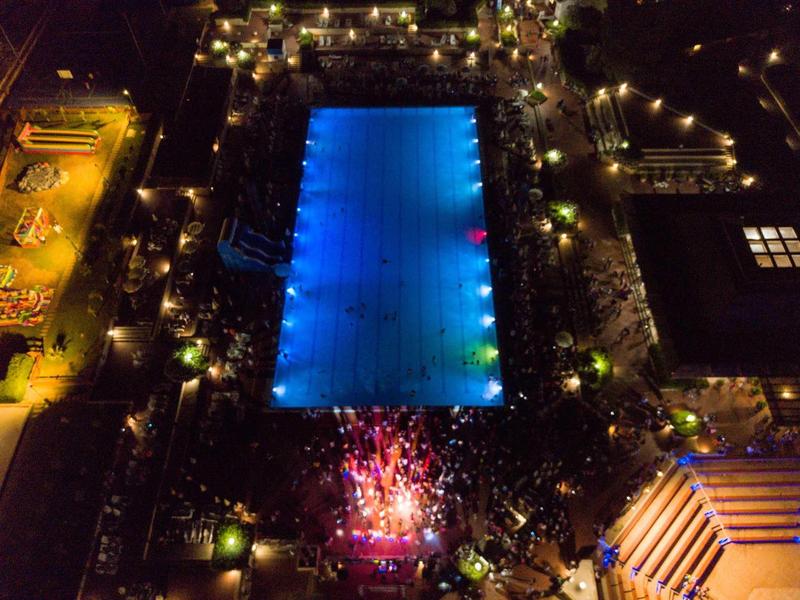 Nocne zdjęcie dużego oświetlonego basenu hotelowego z otaczającymi światłami