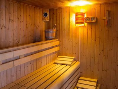 Sauna en bois avec bancs, seau, louche et lumière chaude sur le mur