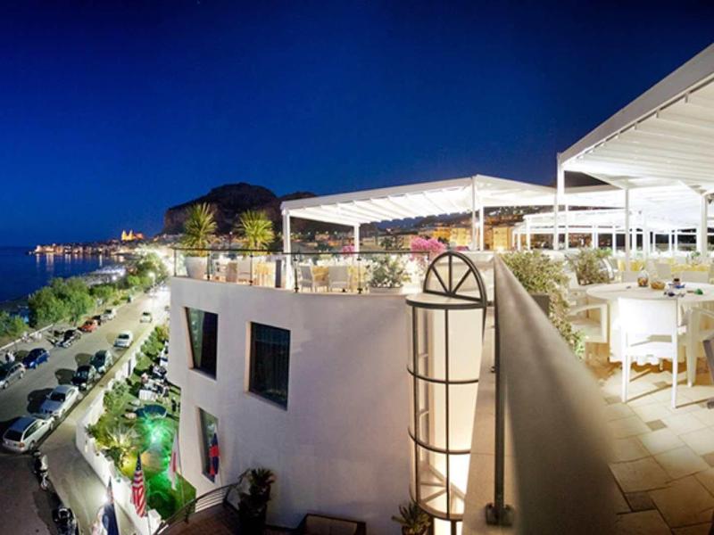Vue en soirée d'une terrasse de restaurant ouverte avec tables et chaises, surplombant une route côtière et la mer.