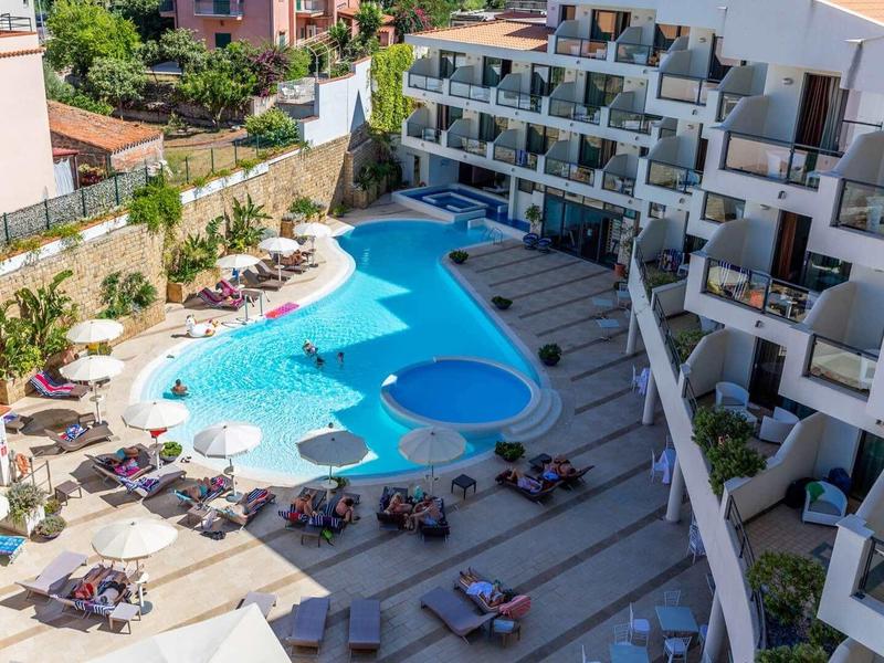 Complexe hôtelier moderne avec piscine extérieure, terrasse ensoleillée et chaises longues autour.
