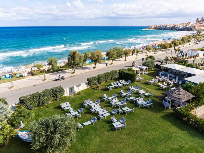 Vue d'une plage ensoleillée avec parc adjacent et transats au bord de la mer.