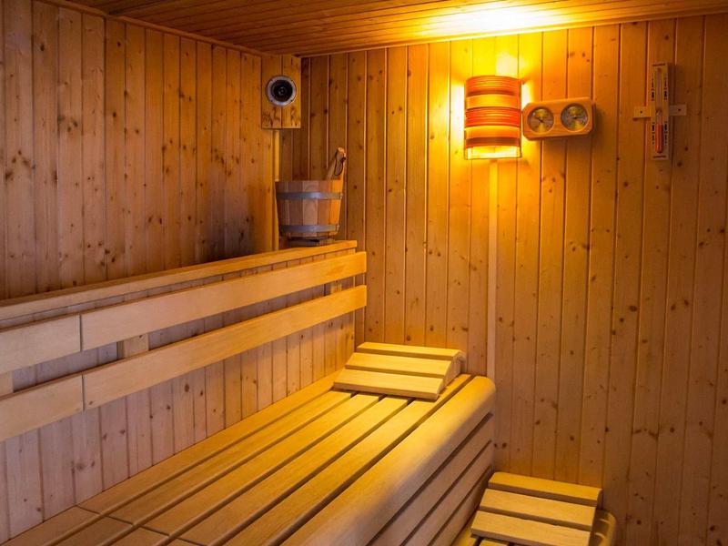 Sauna en bois avec bancs, seau, louche et lumière chaude sur le mur