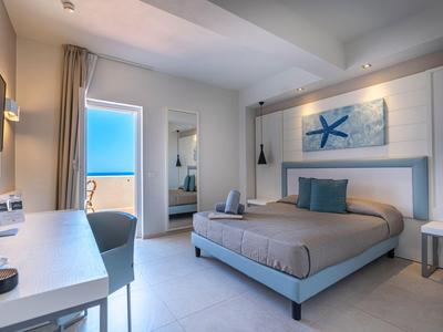 Nowoczesny pokój hotelowy z łóżkiem podwójnym, biurkiem, fotelem i widokiem na morze przez drzwi.