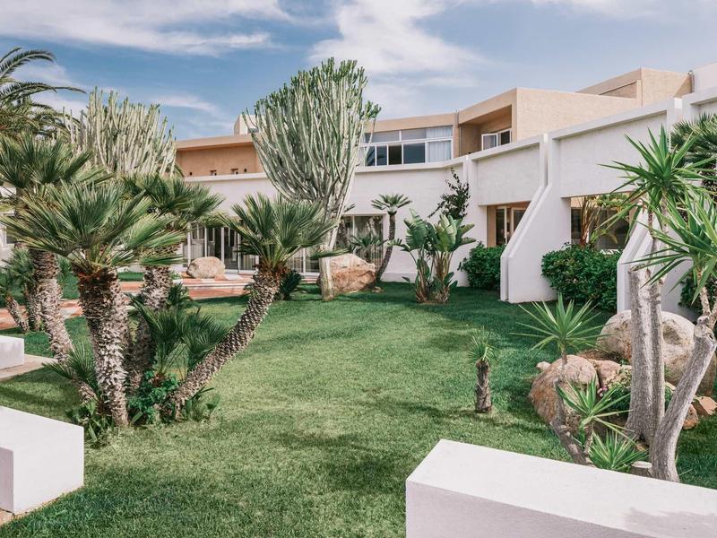 Modern hotel garden with green palms and lush grass under a blue sky.
