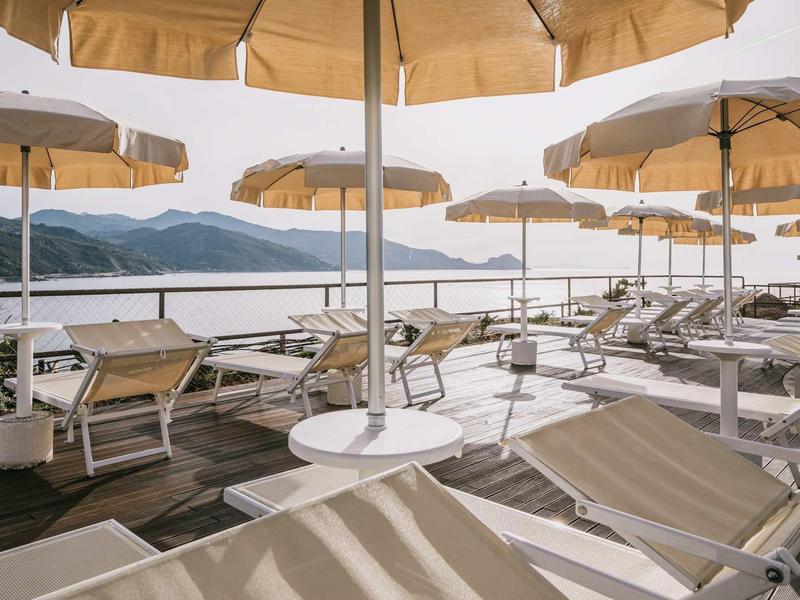 Sun loungers and umbrellas on terrace with sea and mountain view at sunset.