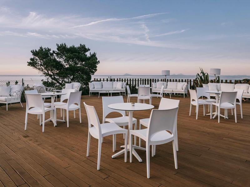 Empty terrace with white chairs and tables overlooking the sea at sunset.