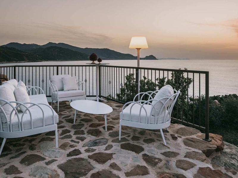 Terrace with white chairs and table overlooking the sea at sunset.