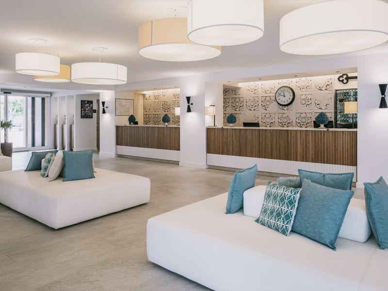 Spacious hotel lobby with modern reception, white seating, and light blue pillows.