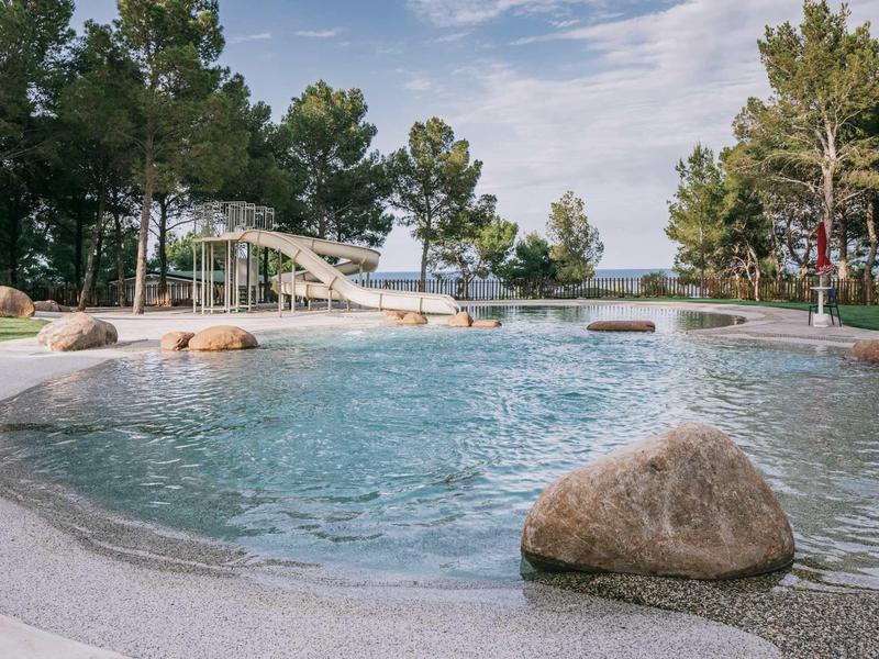 Outdoor pool surrounded by rocks and trees under clear sky with sea view.