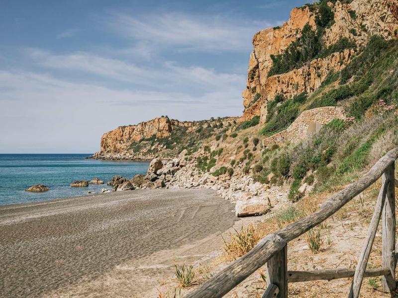 Sandy beach with rocky coast and clear sky, fence in foreground