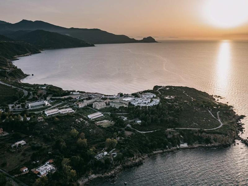 Aerial view of a coastal landscape with buildings and mountains at sunset.