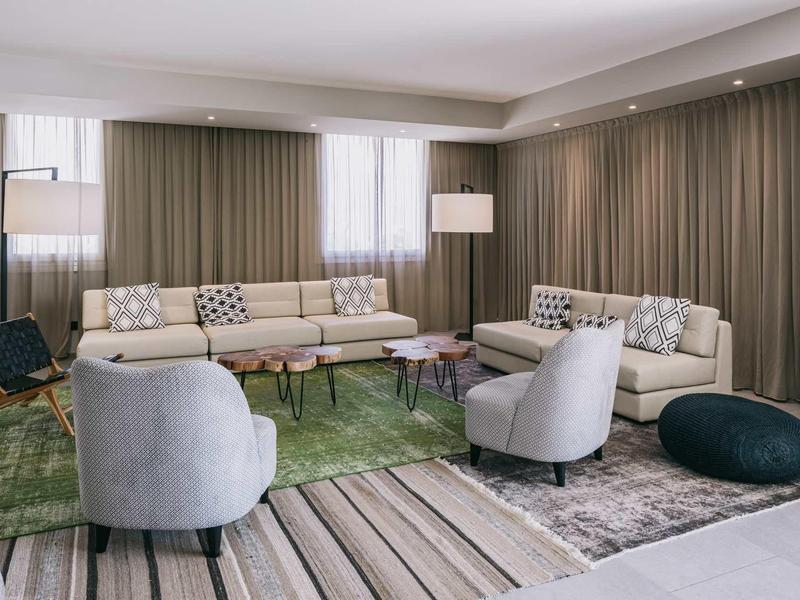 Modern eingerichtetes Wohnzimmer mit zwei Sofas, Sesseln, Teppichen und großen Vorhängen.