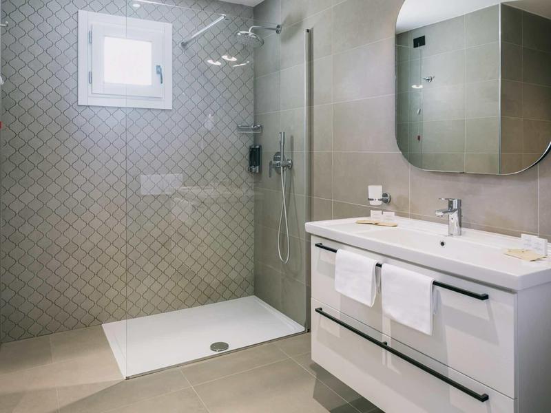 Modernes Badezimmer mit begehbarer Dusche, großem Spiegel und weißem Waschtisch mit Handtüchern.