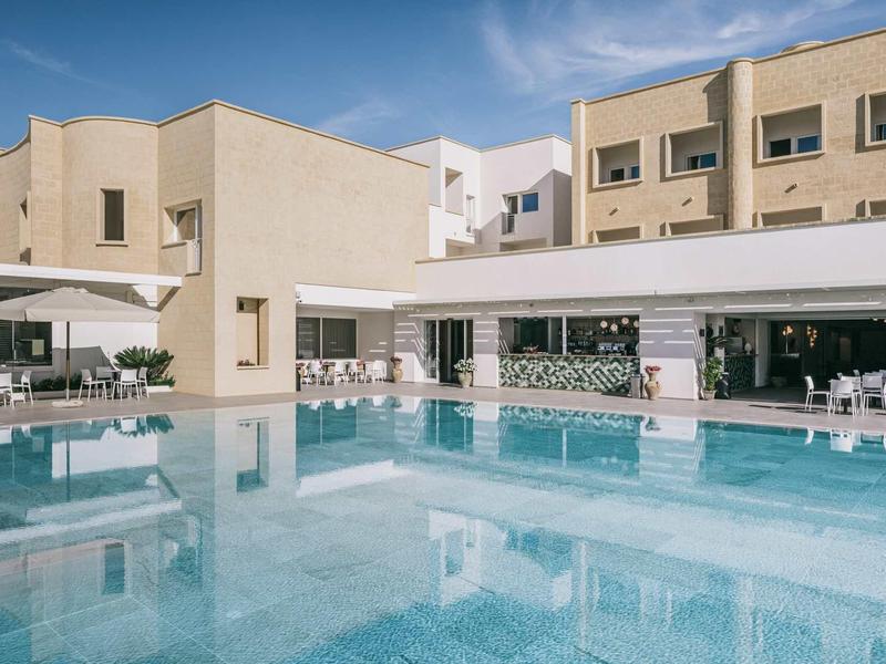 Moderner Hotelpool mit klarblauem Wasser und Liegestühlen unter sonnigem Himmel.