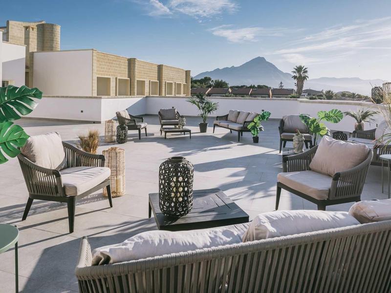 Moderne Dachterrasse mit weißen Möbeln, Pflanzen und Bergblick bei klarem Himmel.