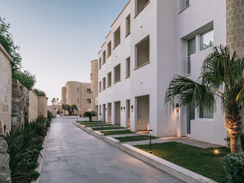 Moderner Wohnkomplex mit weißer Fassade, Grünflächen und Palmen entlang eines Gehwegs.