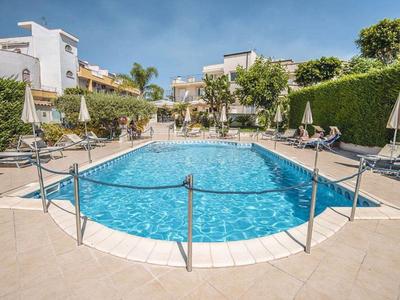 Moderner Poolbereich mit klarem Wasser, Liegestühlen und Sonnenschirmen umgeben von Gebäuden.