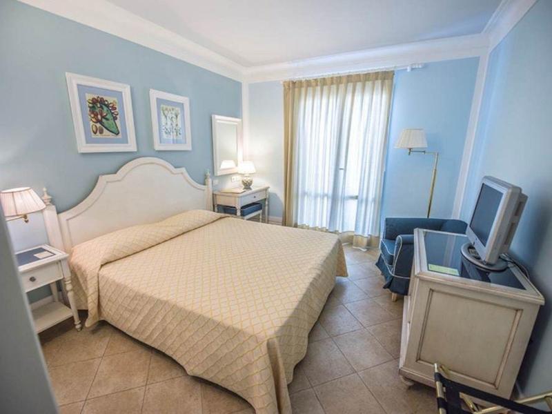 Chambre d'hôtel confortable avec lit double, bureau, télévision et rideau clair devant la fenêtre.