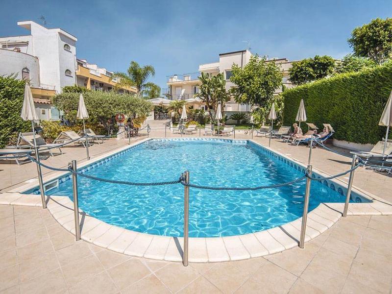 Espace piscine moderne avec eau claire, chaises longues et parasols entouré de bâtiments.