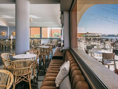 Vnitřní část restaurace s ratanovými židlemi a venkovní část s výhledem na moře za slunečného světla.