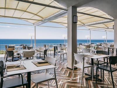 Terasa restaurace s výhledem na moře, prostřené stoly a moderní židle.