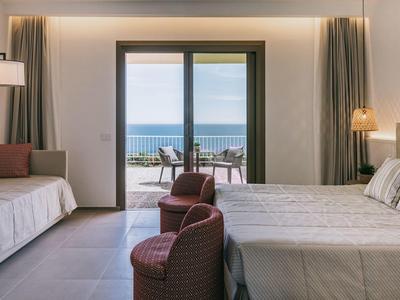 Moderní hotelový pokoj s manželskou postelí, posezením a balkonem s výhledem na moře.