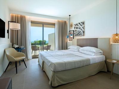 Světý hotelový pokoj s manželskou postelí, křeslem, balkonem a výhledem na moře.