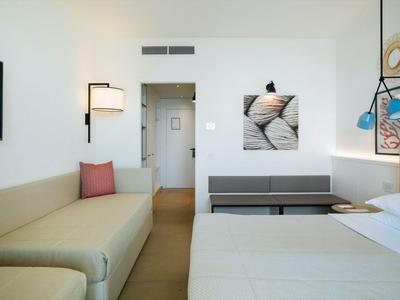 Moderní hotelový pokoj s postelí, pohovkou, nástěnným uměním a minimalistickým designem.