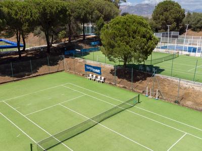 Venku zelený tenisový kurt s stromy a lavičkami v pozadí