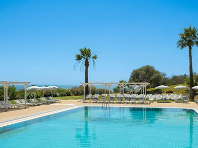 Velký venkovní bazén s slunečníky a palmami pod jasně modrou oblohou