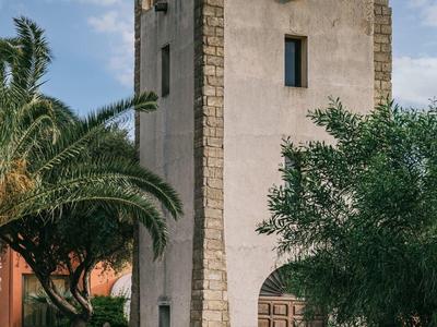 Čtvercová věž s cimbuřím obklopená palmami a zelení v zahradě.