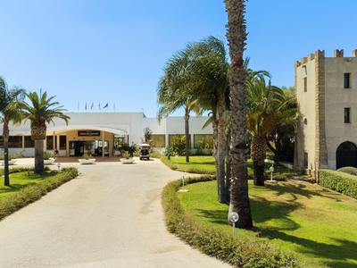 Vjezd do hotelu s palmami a hradbami za jasné oblohy.