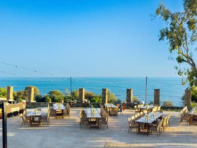 Venkovní terasa s stolky a židlemi s výhledem na moře a jasnou modrou oblohu